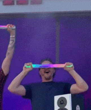a man wearing sunglasses is holding a rainbow colored light up stick over his head