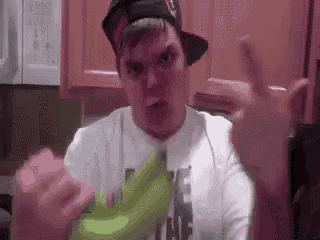a man wearing a hat is holding a banana and giving a middle finger