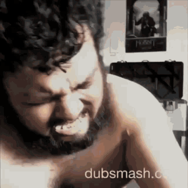 a shirtless man with a beard is making a funny face in front of a poster of the hobbit .