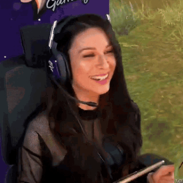 a woman wearing headphones is smiling in front of a sign that says " gaming "