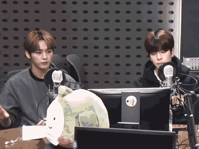 two young men are sitting in front of a computer with a stuffed animal in front of them that has a face on it