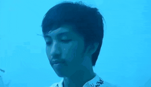 a young man is standing in front of a blue background and looking at the camera .