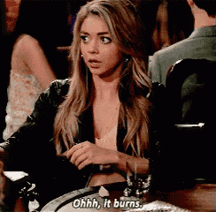 a woman is sitting at a table with a drink and says ohhh it burns .