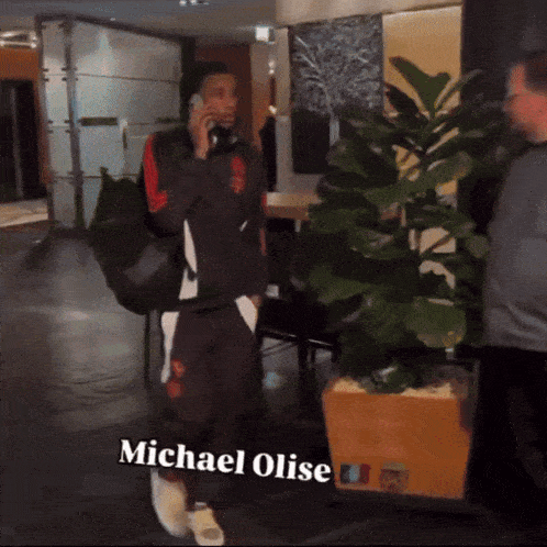 a man talking on a cell phone with the name michael olise on the bottom right