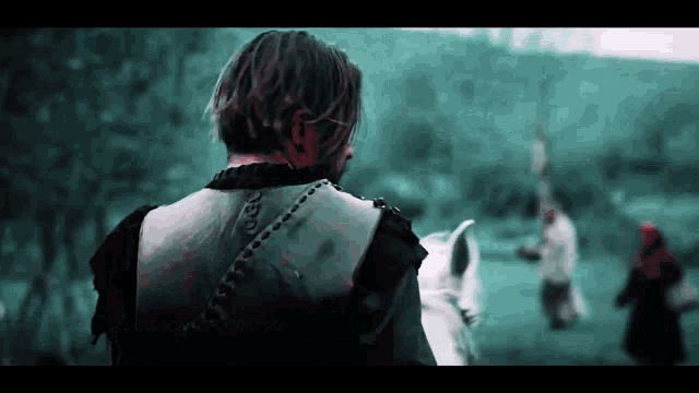 a man in a black vest is riding a white horse in a field