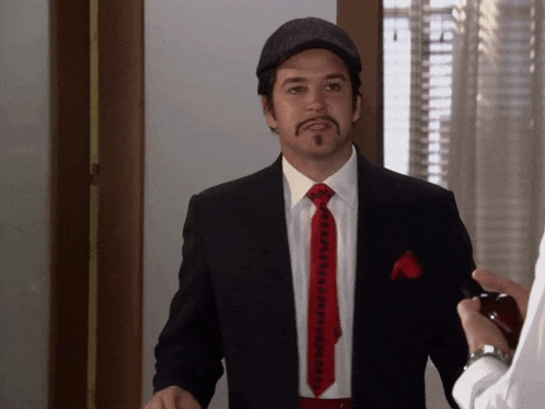 a man in a suit with a red tie and a mustache