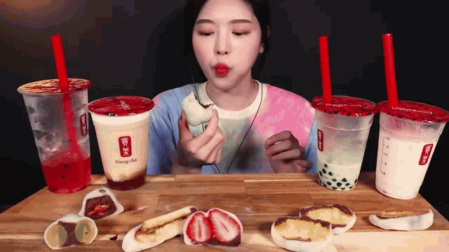 a woman is sitting at a table eating food and drinking from gong cha cups
