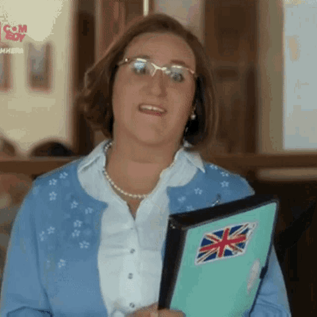 a woman in a blue sweater is holding a folder with a british flag sticker on it