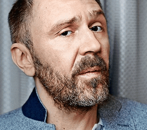 a man with a beard wearing a blue jacket looks at the camera