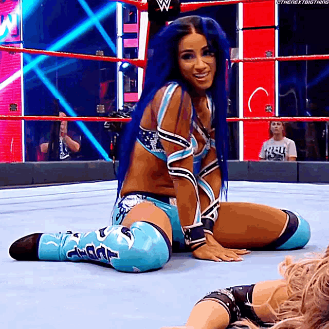a female wrestler with blue hair is kneeling down in a wrestling ring .