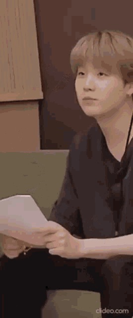 a young man is sitting on a couch holding a piece of paper and looking at it .