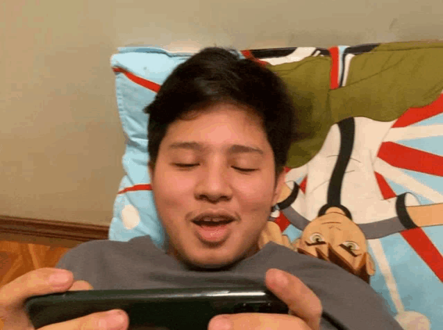 a man laying on a bed holding a cell phone with a cartoon on the pillow behind him
