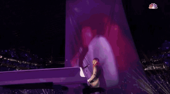a woman singing into a microphone on a stage with a nbc logo in the corner
