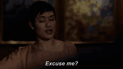 a woman is sitting in a dark room talking to someone and says `` excuse me ? ''