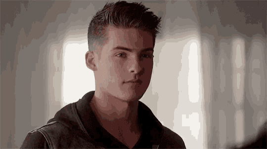 a young man in a black hoodie is looking at the camera in a room .