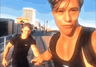 two men are standing next to each other on a sidewalk and one of them is wearing a nike tank top .