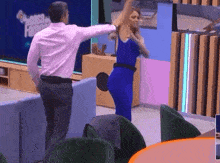 a man in a pink shirt is standing next to a woman in a blue dress who is dancing .