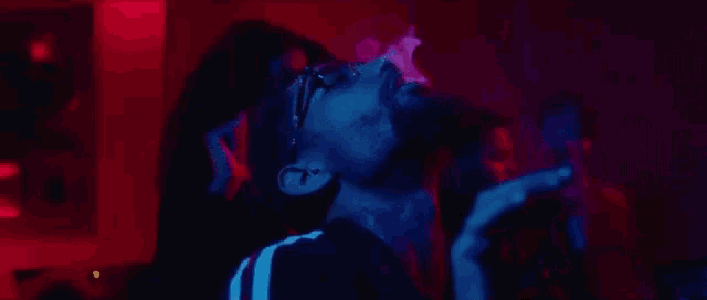 a man with glasses is smoking a cigarette in a dark room with red and blue lights .