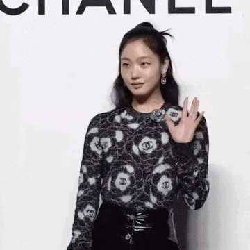 a woman in a black and white sweater is waving her hand in front of a white background .