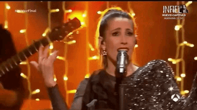 a woman singing into a microphone with a guitar behind her