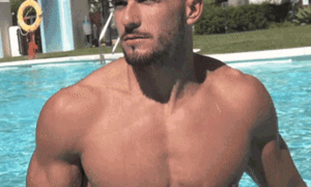 a shirtless man is standing in a swimming pool with a life preserver in the background