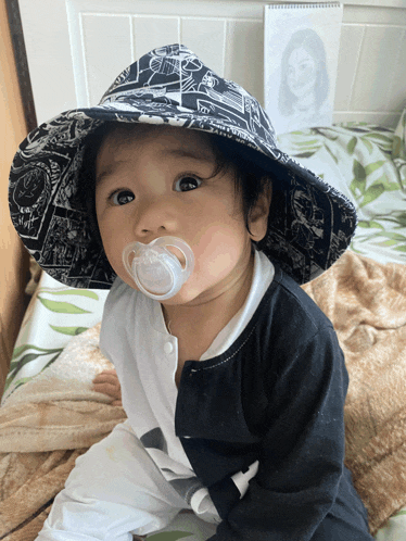 a baby with a pacifier in his mouth wears a black and white hat