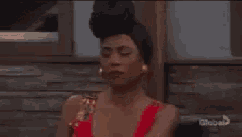 a woman in a red dress is sitting in front of a wooden building and making a funny face .