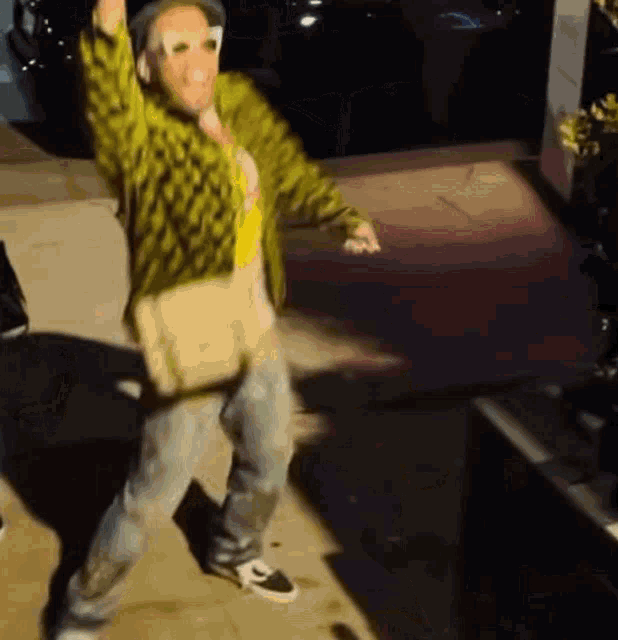 a man in a green jacket and jeans is dancing on the sidewalk .