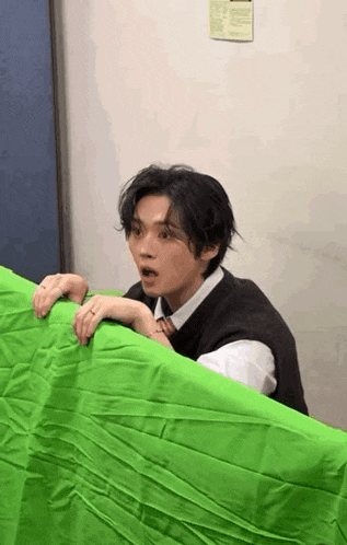 a man is peeking out from behind a green sheet .