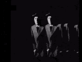 a black and white photo of a group of men in suits and hats standing in a row .