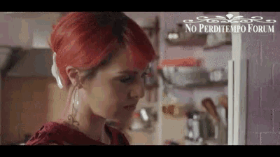 a woman with red hair is standing in front of a purple wall in a kitchen .