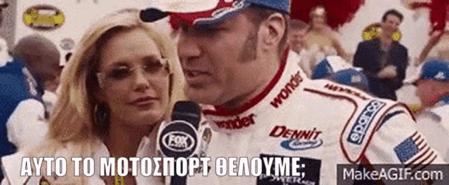 a man in a race car is talking to a woman in front of a crowd .