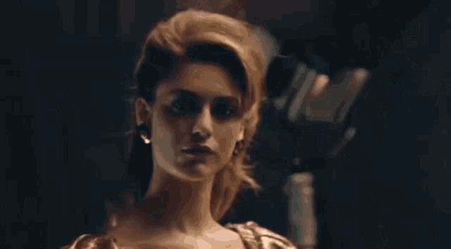 a woman in a dress and earrings is standing in a dark room looking at the camera .