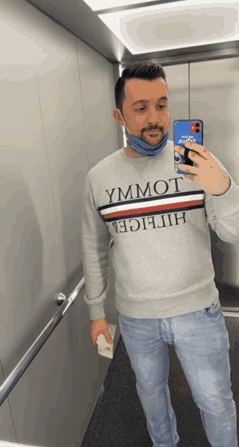 a man wearing a tommy hilfiger sweatshirt takes a selfie