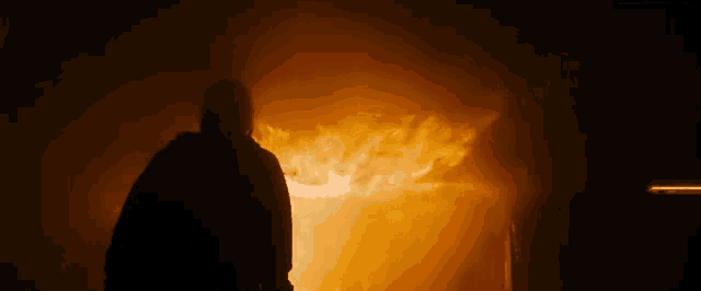 a man is standing in front of a fire in a dark room
