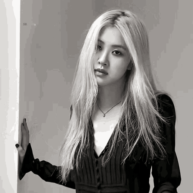 a woman with long blonde hair is leaning against a wall and looking at the camera