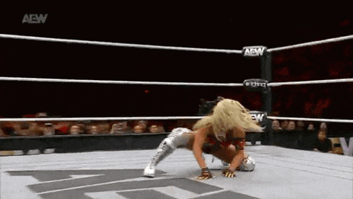 a female wrestler is kneeling down in a wrestling ring while a crowd watches .