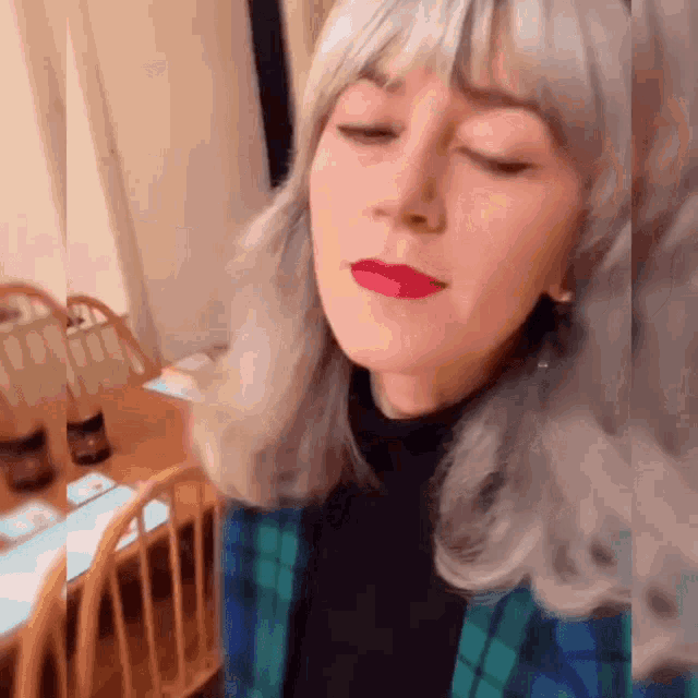 a woman with gray hair is wearing red lipstick and a plaid shirt .