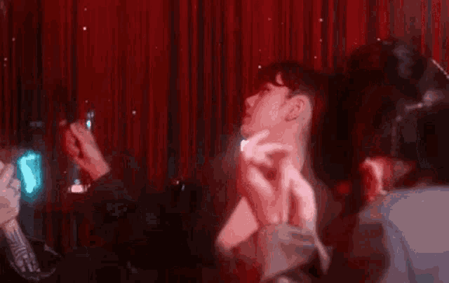 a woman in a suit is dancing in front of a red curtain in a dark room .