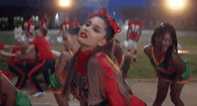 a group of cheerleaders are dancing on a field and one of them has a red bow in her hair