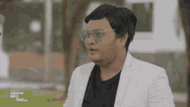 a man wearing sunglasses and a white jacket is standing in a park .