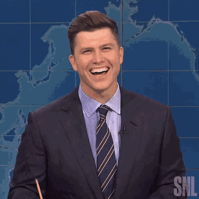 a man in a suit and tie is smiling in front of a snl sign