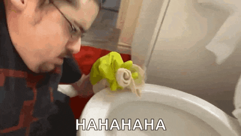 a man is cleaning a toilet with a yellow cloth and the words hahahaha are written on the bottom .