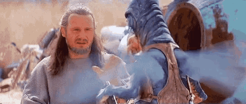 a man with long hair and a beard is standing next to a blue monster in a desert .