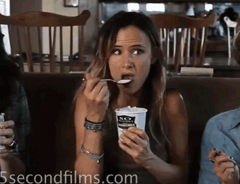 a woman is eating yogurt from a cup that says sq on it
