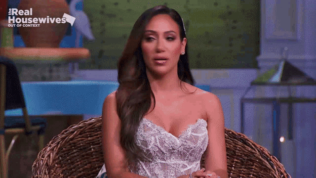 a woman in a white dress is sitting in a wicker chair on a real housewives show .