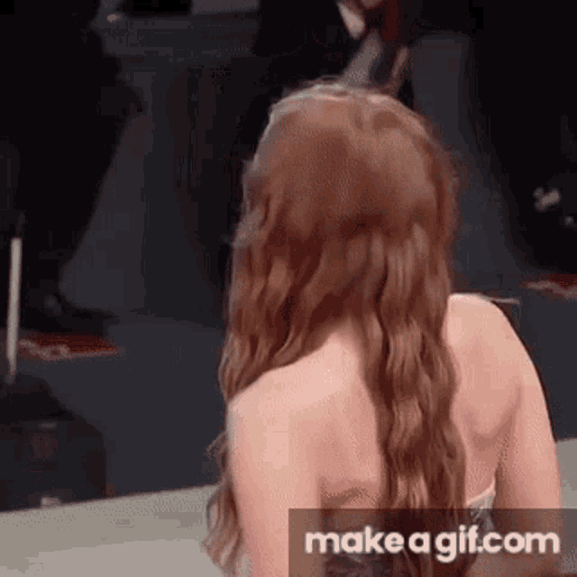 a woman with long red hair is standing on a red carpet and looking at the camera .