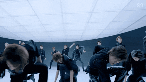 a group of men are dancing in a room with the letter m on the bottom right