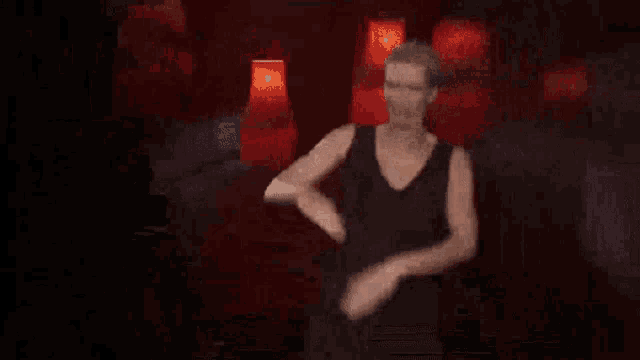 a woman in a black dress is standing in front of a red curtain and clapping her hands .