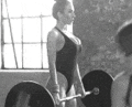 a black and white photo of a woman lifting a barbell in a gym .